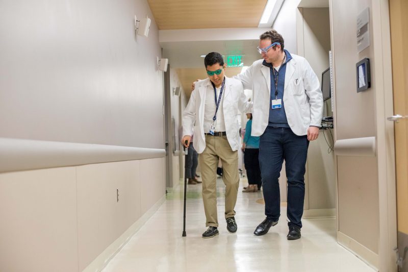 First-year medical student Alexander Tenorio (left) experiences what a patient with glaucoma might by wearing special glasses that replicate macular degeneration. Ross Linker (right) guides Tenorio during geriatrics education at the Kanbar Center at UCSF.